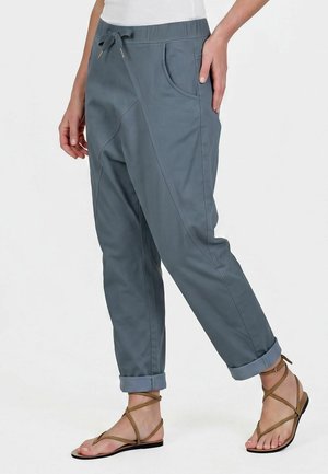 Pantalon décontracté bleu-gris avec taille élastique et cordon, porté roulé aux chevilles, assorti à des sandales plates marron à brides.