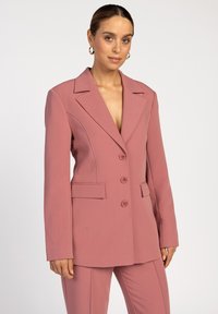 Roze op maat gemaakte blazer met notch-lapels, drie knopen en twee voorzakken. De stof lijkt glad en gestructureerd, geschikt voor formele kleding.