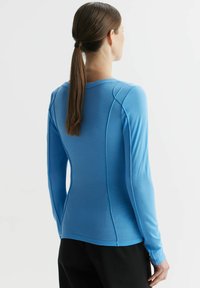 Niebieska koszula z długim rękawem wykonana z miękkiego materiału, z okrągłym dekoltem, dopasowanym krojem i detalami szycia wzdłuż ramion i boków.