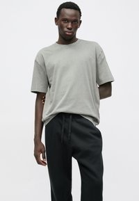 Szara bawełniana koszulka o luźnym kroju, z krótkimi rękawami i okrągłym dekoltem, zestawiona z czarnymi spodniami dresowymi na sznurki.