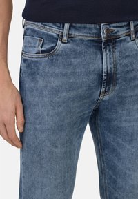 Modre kavbojke iz denima, z zbledelim pranjem, standardnim dizajnom žepov in vidnimi šivi; prikazan slim-fit slog.