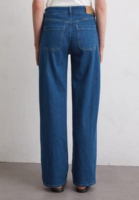 Brede broek van blauwe denim met een gladde textuur, voorzien van twee achterzakken en een bruine leren label aan de taille.