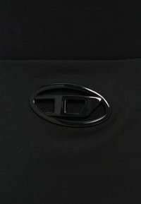 Fekete szövet texturált felülettel, középen az alsó részen egy kiemelkedő fekete ovális logó kivágott mintákkal.