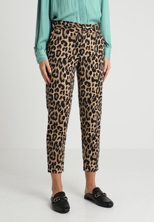 Kvinde iført korte leopardmønstrede bukser, en tealblå bluse med lange ærmer og sorte slip-on loafers med guldkædedetalje.