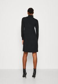 Abito nero a maglia con colletto alto, maniche lunghe e design a sacchetto, caratterizzato da un orlo all'altezza del ginocchio e una texture liscia.