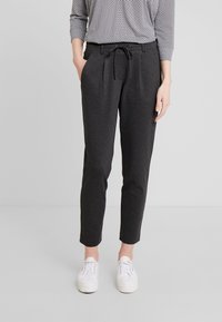 Donkergrijze broek met een geruite patroon, taps toelopende vorm, elastische tailleband met trekkoord, gecombineerd met witte sneakers en een zwart-wit gestreepte top.
