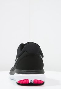 Zapatilla deportiva negra con un upper texturizado, con un diseño elegante, acentos plateados y una suela de goma rosa y blanca.