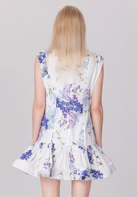 Robe fleurie blanche avec des motifs bleus et violets, manches courtes et ourlet froncé à volants. Fabriquée en tissu léger.