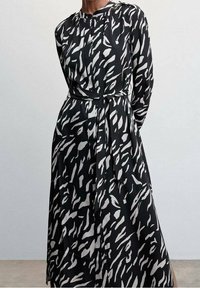 Robe noire avec un motif abstrait blanc, à manches longues, col rond, ceinture à la taille et tissu fluide. Comprend des éléments de design verticaux.