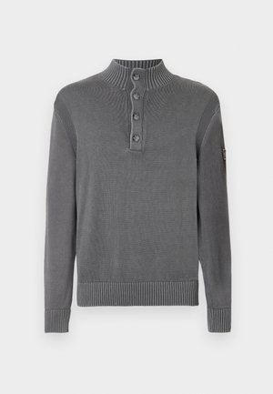 Grå stickad tröja med ribbad hög krage, fyra-knapps knappslå, långa ärmar samt ribbade ärmslut och fåll mot en vit bakgrund.