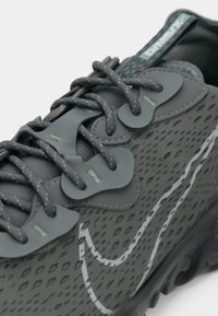 Scarpa da ginnastica grigia con una parte superiore testurizzata, lacci coordinati, sovrapposizioni flessibili e un distinto logo swoosh bianco sul lato.