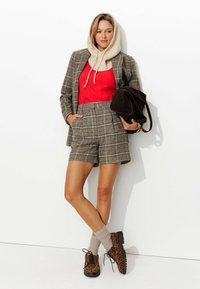 Blazer à carreaux marron sur un haut rouge, capuche beige et shorts à carreaux. Les accessoires comprennent un sac marron et des chaussures à imprimé léopard avec des chaussettes beiges.