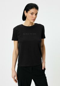Sort bomulds T-shirt med rund hals og korte �ærmer, med teksten "Gør hvad du elsker" trykt i en diskret grå farve på brystet.