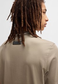 Camicia khaki a maniche corte con vestibilità rilassata, caratterizzata da una leggera trama e un'etichetta nera "HUGO" posizionata sul retro del collo.