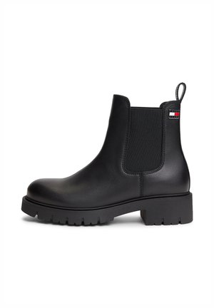 Schwarzer Leder-Knöchelstiefel mit elastischen Seitenteilen, dicker profillierter Sohle, Zuglasche und kleinem Tommy Hilfiger Logo nahe dem oberen Rand auf der Außenseite.