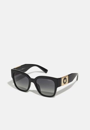 Schwarze rechteckige Sonnenbrille mit grauen Verlaufsgläsern, markantem Rahmen und goldfarbenen Elementen, die ein detailliertes Logo an den Scharnieren aufweisen.