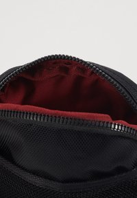Geantă din material textil negru, cu un strat exterior texturat și interior roșu, având un fermoar rezistent în partea de sus pentru închidere.