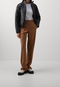 Black puffer jacket with logo pattern, gray t-shirt, and brown wide-leg trousers. Chunky white and black shoes. Smooth texture throughout.