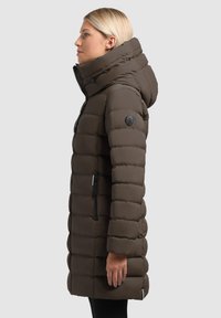 Brązowa kurtka puchowa z kapturem, charakteryzująca się pikowanym wzorem, bocznymi kieszeniami na zamek oraz odznaką na lewym rękawie. Gładka, matowa powierzchnia.