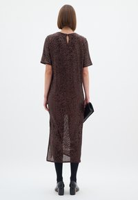 Barna flitteres ruha rövid ujjakkal, közepes hosszúságú, kulcslyuk hátkivágással, fekete harisnyával és magassarkú cipővel viselve, fekete clutch táskával.