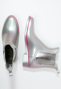Bottines argentées avec une finition lisse et brillante. Présentent un bord rose au niveau de la semelle et une languette pour faciliter l'enfilage.