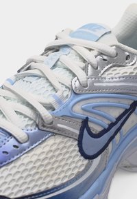 Biela a svetlomodrá teniska Nike s sieťovinovým materiálom, polstrovaným jazykom a detailným viazaním. Logo Nike Swoosh v námorníckej modrej na boku.