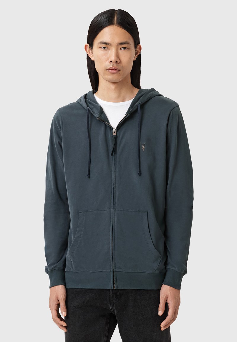 Felpa con cappuccio e zip di colore verde scuro, realizzata in tessuto morbido, con chiusura frontale a zip, cordini e due tasche anteriori. Accentata con un logo.