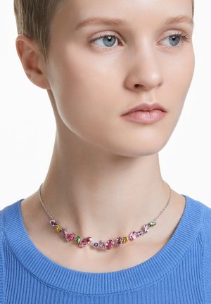 Multicolored gem necklace with pink, purple, and green stones, set in a silver chain, worn against a light blue ribbed top.