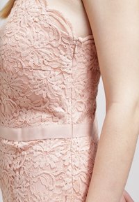 Lichtroze kanten jurk met bloemenpatronen, een zachte textuur, een ritssluiting aan de zijkant en een satijnen tailleband.