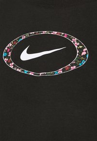 Musta t-paita, jossa on suuri valkoinen Nike-logo, jota ympäröi vaaleanpunainen ja sininen kukkakuosi. Valmistettu pehmeästä, hengittävästä kankaasta.