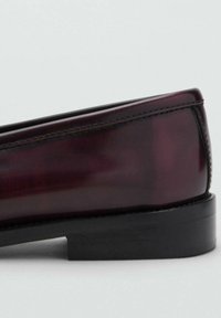 Burgundy leather loafers with a glossy finish, featuring a sleek, rounded shape and a black, low-profile sole, detailed with subtle stitching.