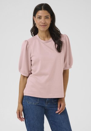 Light pink short-sleeve top with puffed sleeves and crew neckline. Made of soft fabric, paired with blue denim jeans, showing a relaxed fit.