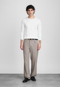 Long-sleeve white cotton T-shirt with round neck, paired with light gray plaid trousers and a black belt with a gold buckle, worn with black shoes.