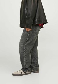 Chaqueta de cuero negra, camisa de cuadros roja debajo, vaqueros de mezclilla gris holgados y zapatillas beige con acentos oscuros. Atuendo casual con estilos en capas.