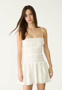 Weißes Sommerkleid mit einem figurbetonten, gerafften Oberteil mit Rüschen und einem schwingenden, kurzen Rock. Glattes, leichtes Material mit strukturierten Details.