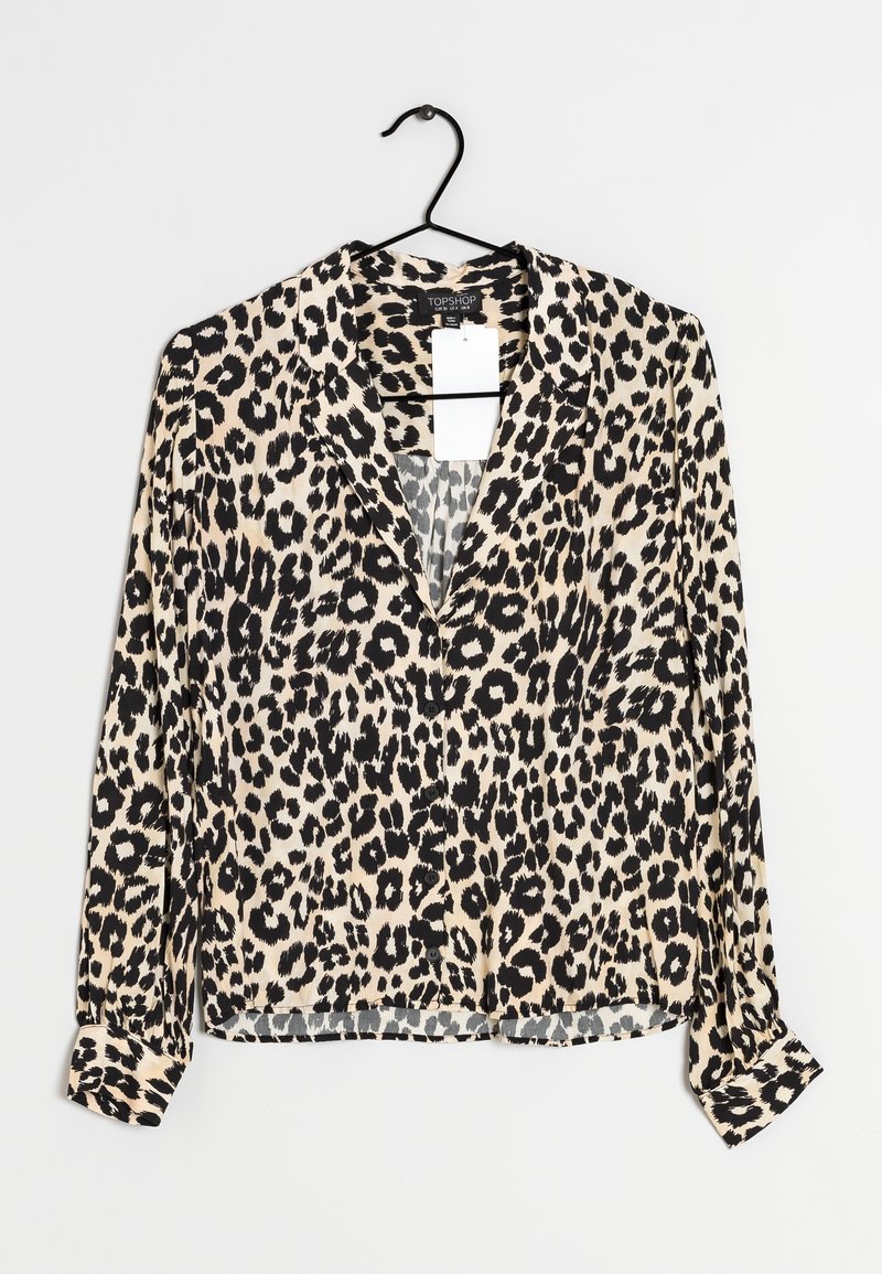 Leopardenmuster-Bluse mit langen Ärmeln, V-Ausschnitt, weichem Stoff, hellbeigem Hintergrund und schwarzen Flecken. Hat knöpfbare Manschetten und einen Aufhänger.