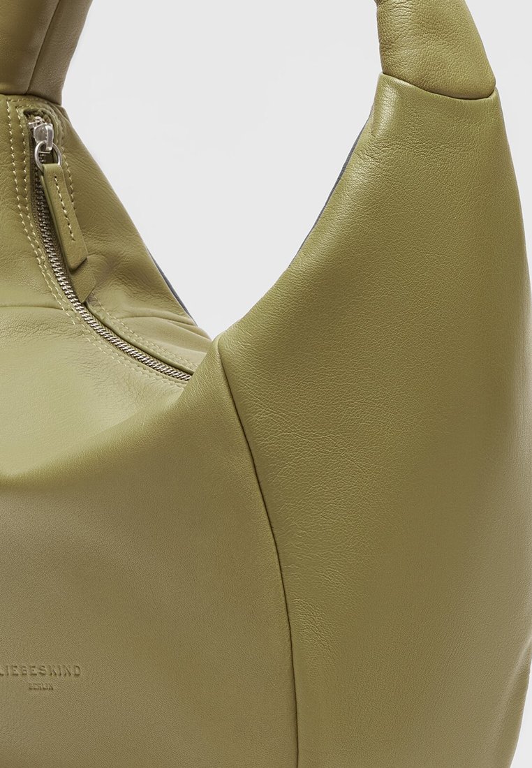 Grüne Lederhandtasche mit sichtbarem Reißverschluss und geprägtem Markennamen auf glatter Oberfläche vor einem hellen Hintergrund.