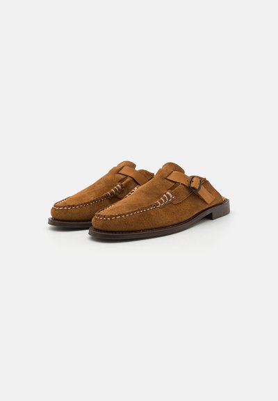 Scarpe slip-on in suede marrone con punta rotonda, cinturino in pelle, fibbia e cuciture in contrasto sulla parte superiore per un dettaglio aggiuntivo.