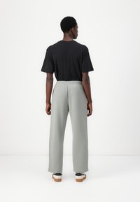 Sort kortærmet t-shirt parret med lysegrå, løstsiddende sweatpants. Bukserne har en elastisk talje og er lavet af blødt stof.