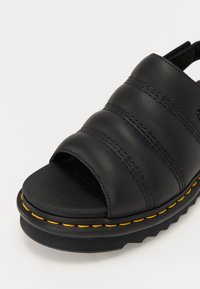 Zwarte leren sandaal met drie horizontale stripes, open teen en een gele stiksels rond de zool. Gestructureerde voetbed en afgerond ontwerp.
