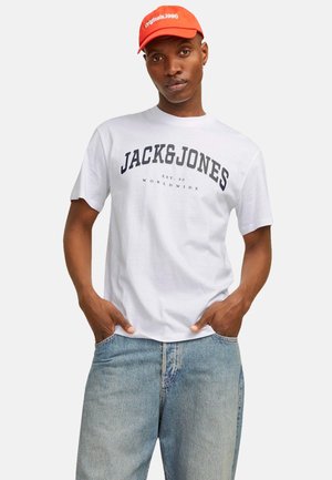 T-shirt bianca in cotone con testo audace in blu navy "JACK & JONES" e "EST. 90 WORLDWIDE." Abbinato a jeans in denim azzurri e un cappellino arancione.