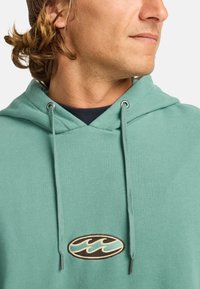 Light teal hoodie featuring a rounded neckline, silver eyelets, and a prominent embroidered logo in dark brown and teal.