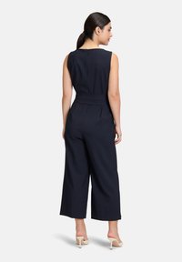 Marinblå jumpsuit med ärmlös design, bälte i midjan, vida byxor och dold dragkedja bak. Slät tygstruktur.