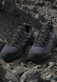 Svarta och grå vandringsskor med en texturerad mesh-övre, solid gummisula och tre randiga detaljer. Har förstärkt tå och snöröglor.