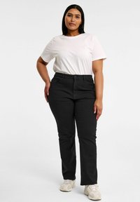 Mustat korkea vyötäröiset housut, joissa on sileä pinta, litteä etuosa ja viisi taskua, yhdistettyinä yksinkertaiseen valkoiseen lyhythihaiseen t-paitaan.