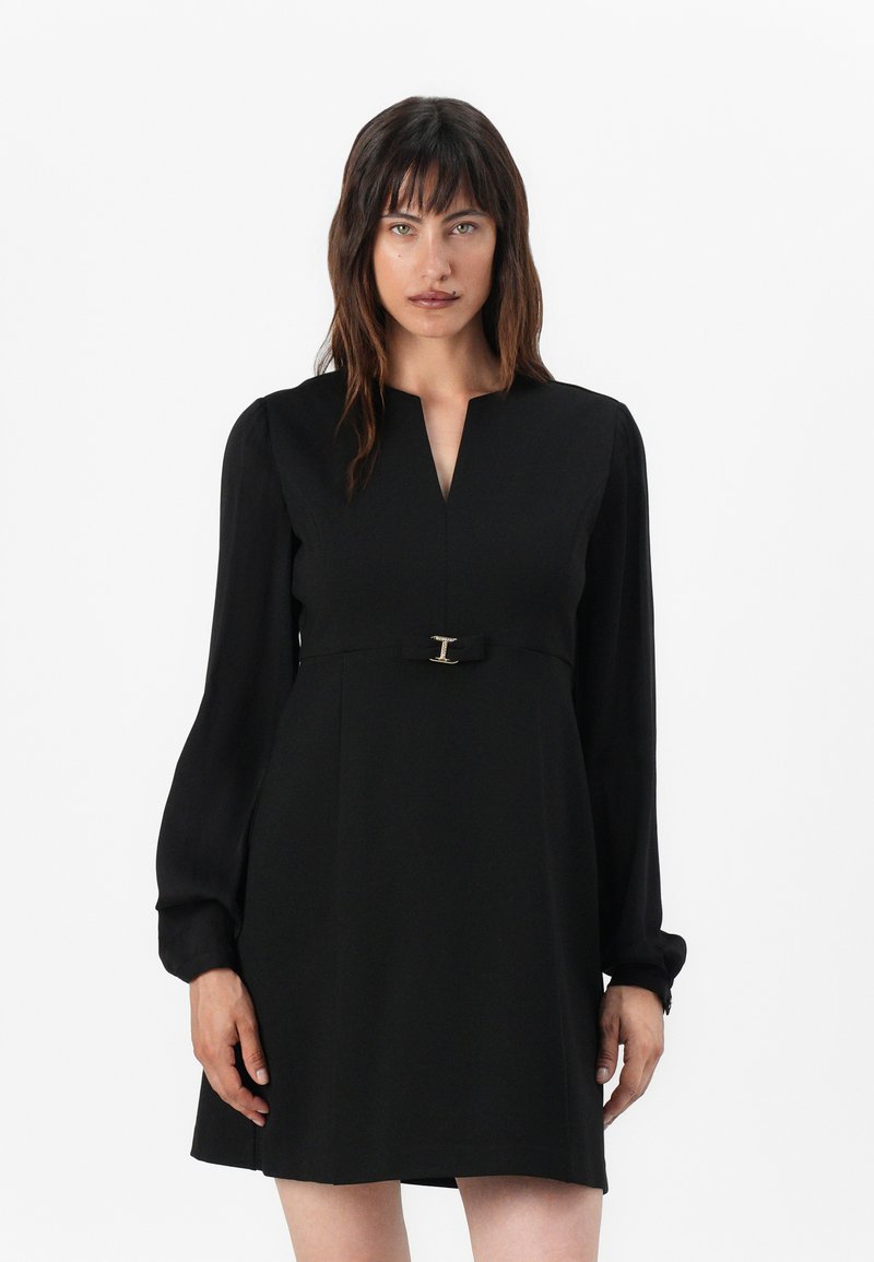 Abito nero con scollatura a V e maniche a sbuffo lunghe. Presenta un corpino aderente, gonna a trapezio e un dettaglio in metallo argentato in vita.