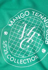 Zelená látka s grafikou na tenisové téma. Obsahuje bílý text: "MANGO TENNIS CLUB" a "S/S 23 COLLECTION", spolu s mřížkovým vzorem a tenisovými ikonami.