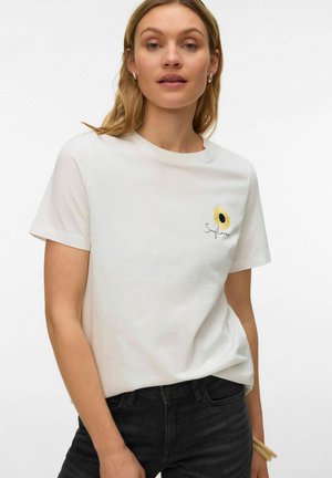 Woman wearing white t-shirt with small sunflower graphic and "Sunflower" text, paired with black jeans, standing against plain white background.
