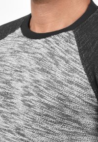 Sudadera de punto gris y negra con un cuerpo texturizado, que presenta mangas raglán en negro sólido y un cuello redondo.
