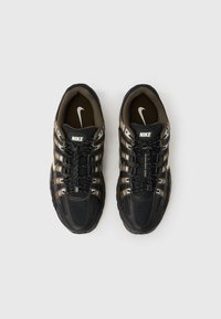 „Nike“ sportbačiai su juodu ir rudu tinklelio viršumi, tekstūruota gumine padu, atspindinčiomis detalėmis ir užtikrinta raištelių sistema.